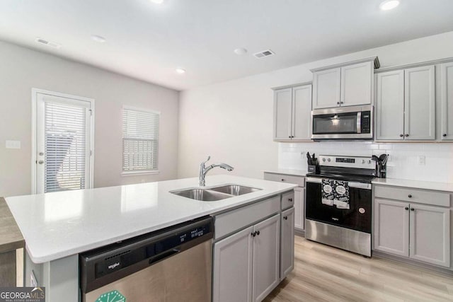 kitchen featuring a kitchen island with sink, sink, stainless steel appliances, and gray cabinetry