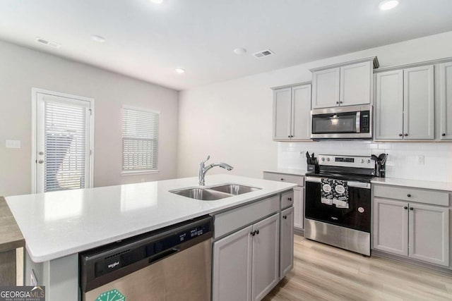 11948 Brightside Pkwy, Hampton, GA 30228 - kitchen featuring appliances with stainless steel finishes, gray cabinets, a kitchen island with sink, light wood-style flooring, and tasteful backsplash
