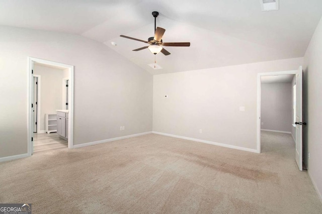 unfurnished bedroom featuring lofted ceiling, ensuite bath, light colored carpet, and ceiling fan