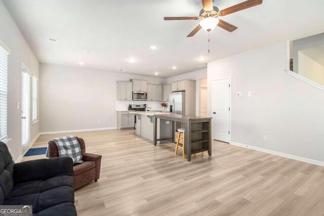 kitchen featuring light hardwood / wood-style floors, stainless steel appliances, a center island with sink, and ceiling fan