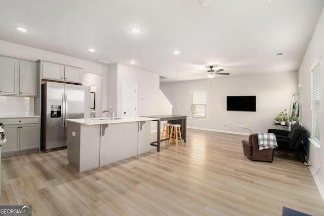 kitchen with gray cabinetry, light hardwood / wood-style flooring, a center island with sink, stainless steel fridge, and a kitchen breakfast bar