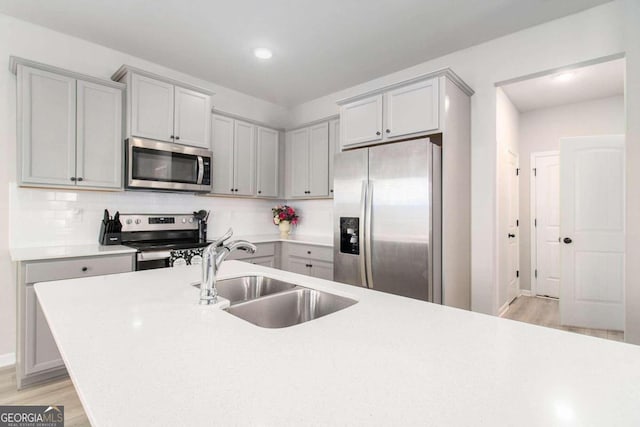 kitchen with appliances with stainless steel finishes, sink, backsplash, and light hardwood / wood-style flooring