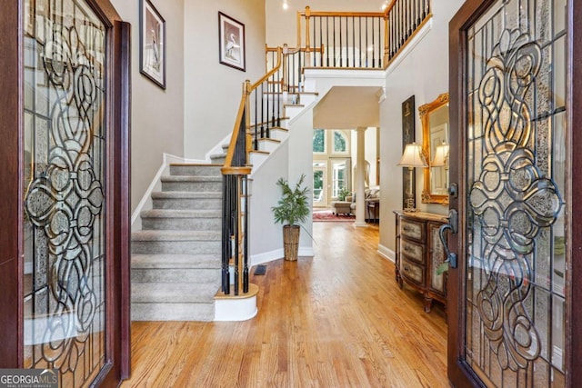 entrance foyer with decorative columns, a high ceiling, and light wood-type flooring