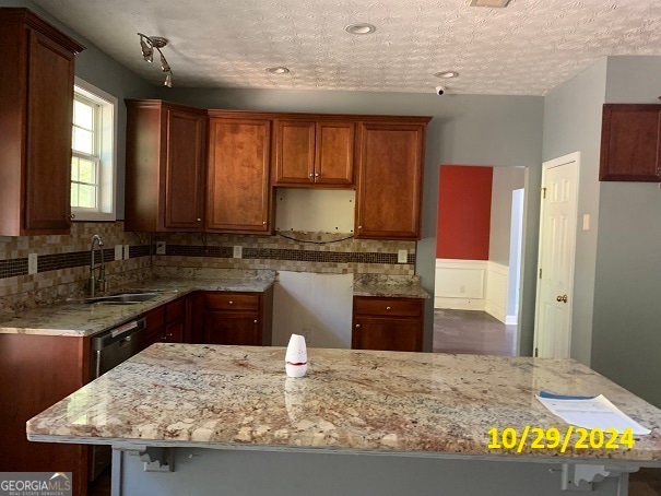 kitchen with light stone countertops, sink, a textured ceiling, decorative backsplash, and a breakfast bar area