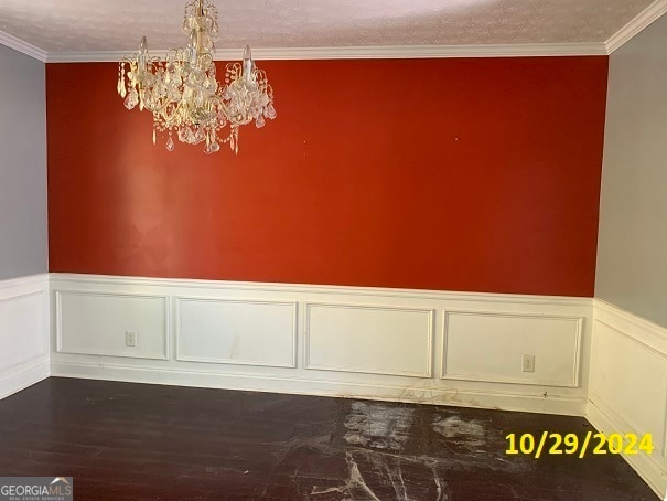 empty room with ornamental molding, a notable chandelier, and hardwood / wood-style flooring