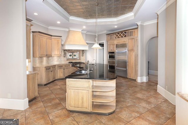kitchen with built in refrigerator, a raised ceiling, a sink, custom exhaust hood, and decorative backsplash