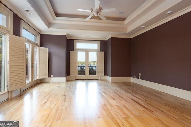 empty room with a tray ceiling, wood finished floors, a ceiling fan, and ornamental molding