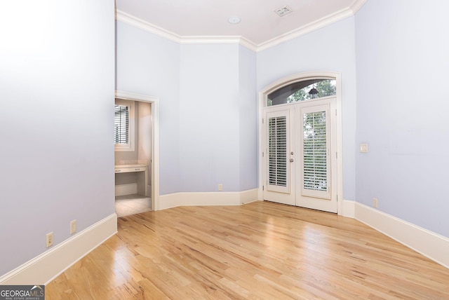 spare room with healthy amount of natural light, wood finished floors, ornamental molding, baseboards, and french doors
