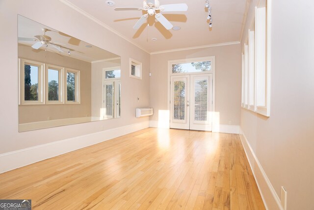 spare room featuring a ceiling fan, plenty of natural light, wood-type flooring, baseboards, and crown molding