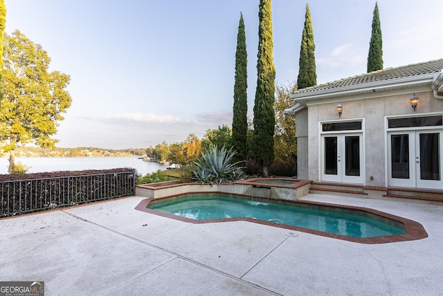 swimming pool with french doors, an in-ground hot tub, a patio, and a water view