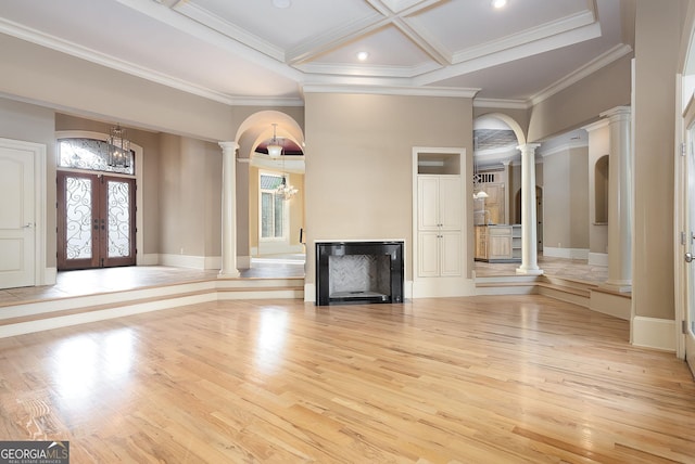 unfurnished living room featuring ornate columns, light wood-style flooring, a chandelier, french doors, and crown molding