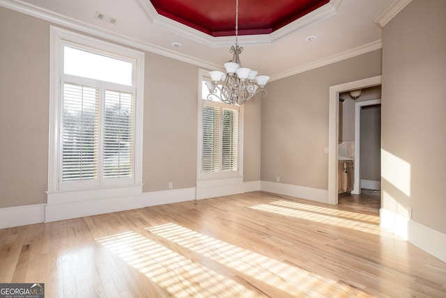spare room with a raised ceiling, hardwood / wood-style flooring, a chandelier, ornamental molding, and baseboards