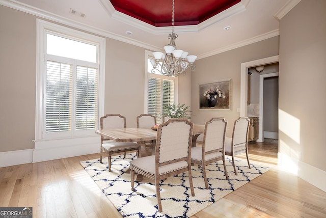 dining room featuring a raised ceiling, healthy amount of natural light, wood-type flooring, and crown molding