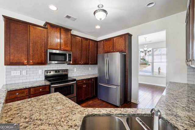 kitchen with an inviting chandelier, light stone countertops, stainless steel appliances, and dark hardwood / wood-style flooring