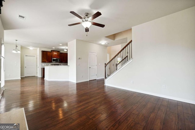 unfurnished living room with ceiling fan with notable chandelier and dark hardwood / wood-style floors