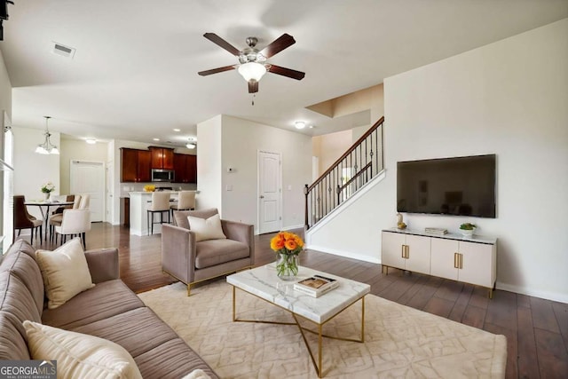 living room featuring ceiling fan with notable chandelier and dark hardwood / wood-style flooring