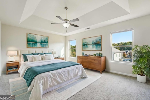 carpeted bedroom featuring ceiling fan, a raised ceiling, and multiple windows