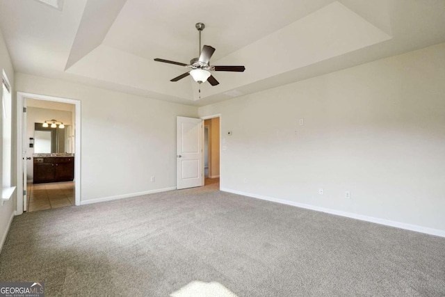 unfurnished bedroom featuring carpet flooring, ceiling fan, a tray ceiling, and ensuite bath