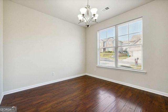 spare room featuring an inviting chandelier and dark hardwood / wood-style flooring