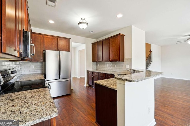 kitchen with light stone countertops, appliances with stainless steel finishes, dark hardwood / wood-style flooring, kitchen peninsula, and decorative backsplash