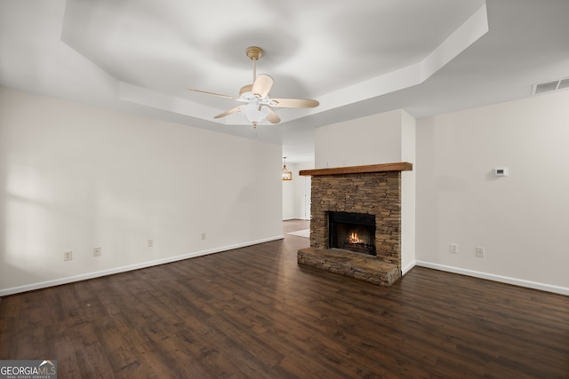 unfurnished living room featuring dark wood-type flooring, ceiling fan, a fireplace, and a raised ceiling