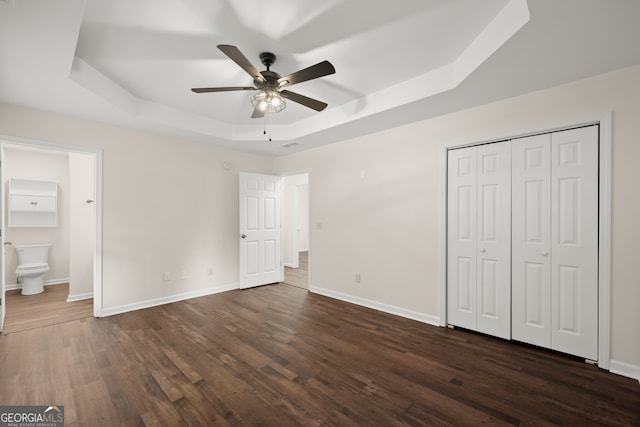 unfurnished bedroom featuring a raised ceiling, dark hardwood / wood-style flooring, a closet, ceiling fan, and connected bathroom