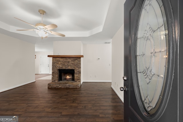 unfurnished living room featuring dark wood-type flooring, ceiling fan, a raised ceiling, and a fireplace