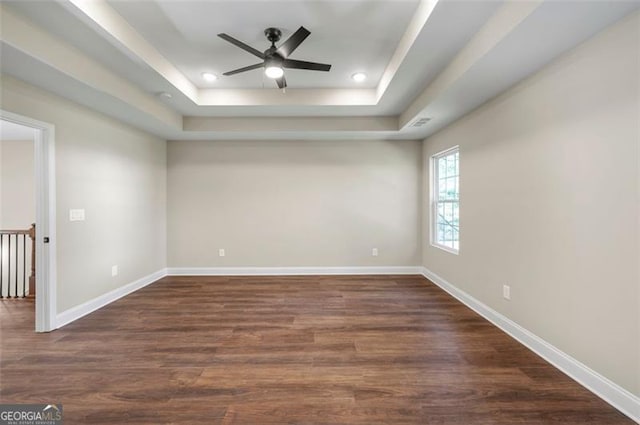 spare room with dark wood-type flooring, ceiling fan, and a raised ceiling