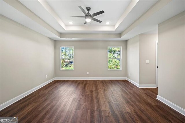 unfurnished room with a healthy amount of sunlight, dark hardwood / wood-style floors, and a tray ceiling