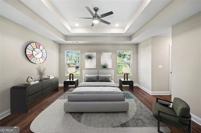 bedroom with dark hardwood / wood-style flooring, a raised ceiling, and ceiling fan