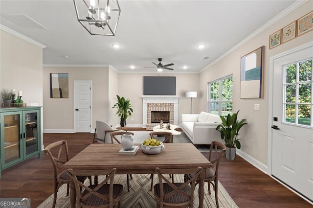 dining space featuring crown molding, dark hardwood / wood-style flooring, ceiling fan with notable chandelier, and a brick fireplace