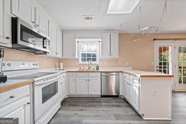 kitchen with light wood-type flooring, stainless steel appliances, kitchen peninsula, and white cabinets