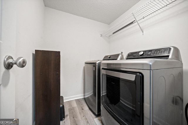 laundry area with washer and dryer, a textured ceiling, and light hardwood / wood-style floors