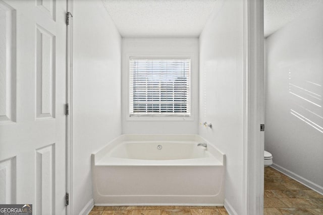 bathroom with a bath, a textured ceiling, and toilet