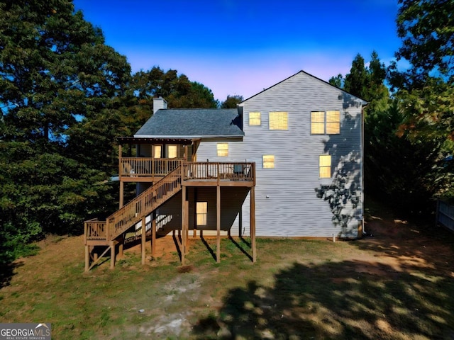 back house at dusk with a wooden deck and a yard