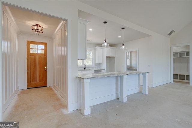 kitchen with light stone countertops, white cabinetry, hanging light fixtures, and lofted ceiling