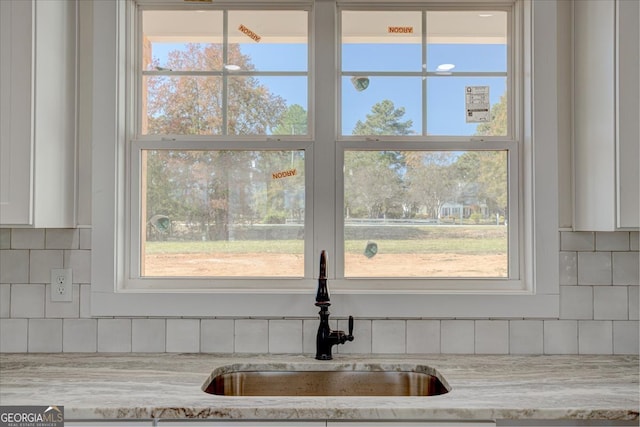 details featuring backsplash, light stone countertops, sink, and white cabinets