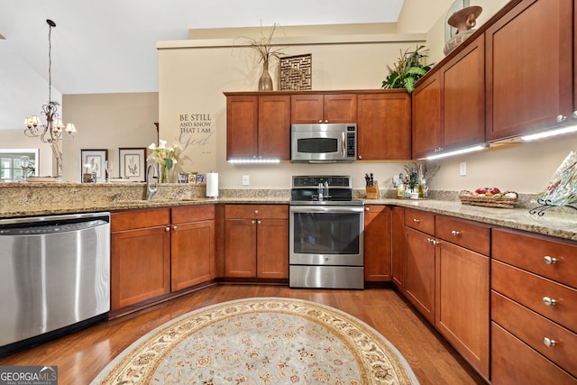 kitchen with light stone countertops, appliances with stainless steel finishes, hardwood / wood-style flooring, and hanging light fixtures