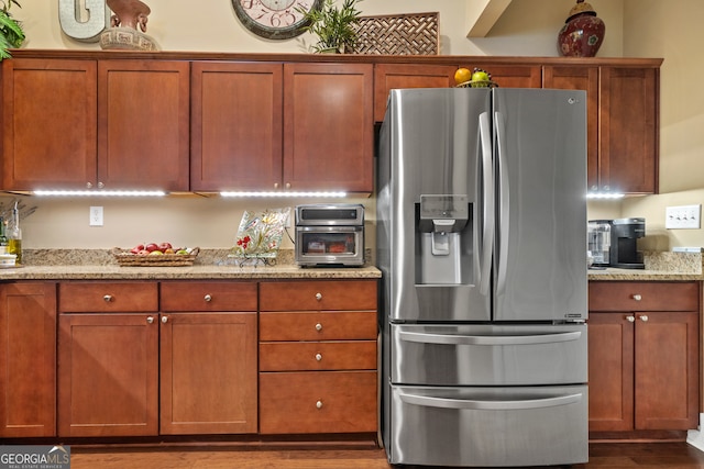 kitchen featuring hardwood / wood-style flooring, stainless steel fridge, and light stone counters