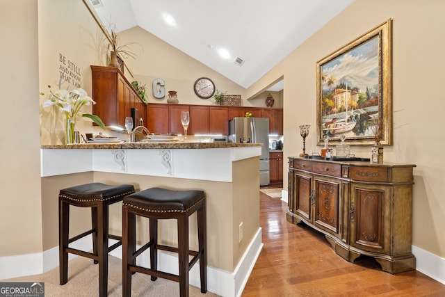 kitchen featuring kitchen peninsula, a kitchen breakfast bar, light hardwood / wood-style flooring, stainless steel fridge, and vaulted ceiling