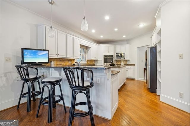 kitchen featuring light hardwood / wood-style flooring, backsplash, decorative light fixtures, white cabinets, and appliances with stainless steel finishes