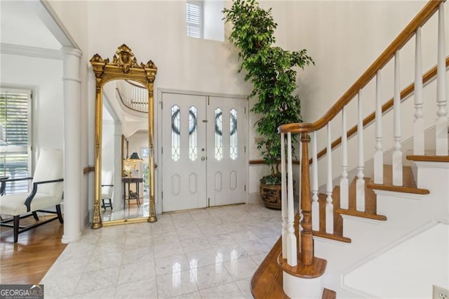 entrance foyer with ornate columns, a towering ceiling, and ornamental molding