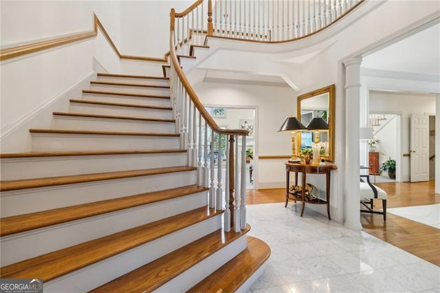 stairs with a towering ceiling, hardwood / wood-style flooring, and ornate columns