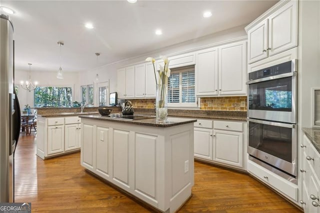 kitchen with kitchen peninsula, wood-type flooring, stainless steel appliances, and a kitchen island