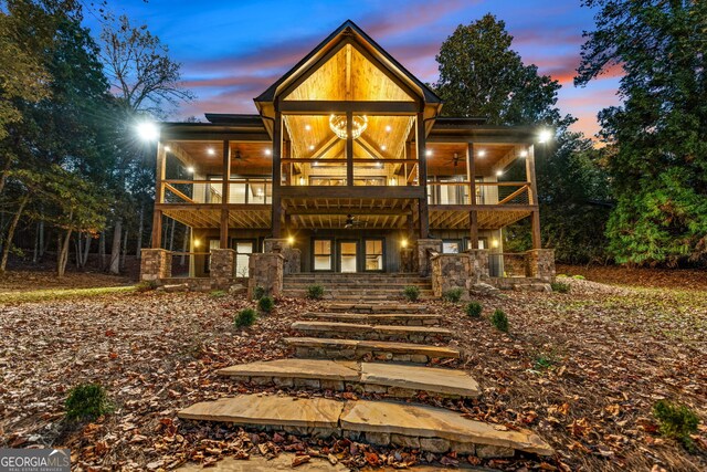 back house at dusk featuring a balcony and ceiling fan