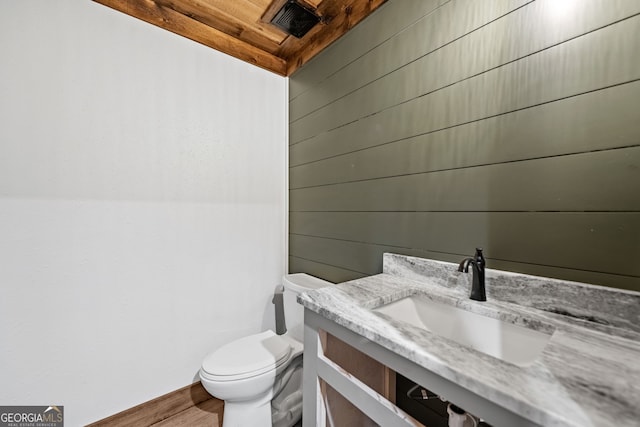 bathroom featuring toilet, wooden walls, wood ceiling, and vanity