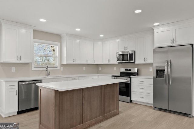 kitchen featuring stainless steel appliances, sink, light hardwood / wood-style flooring, white cabinets, and a kitchen island