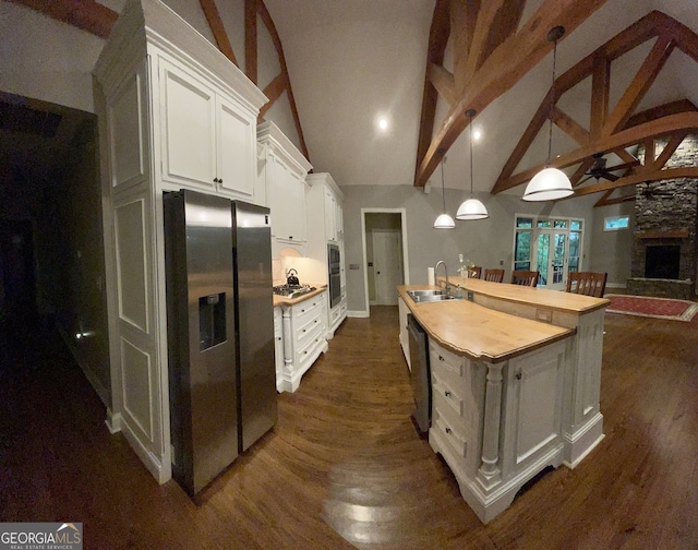 kitchen with hanging light fixtures, stainless steel appliances, a center island with sink, sink, and white cabinetry