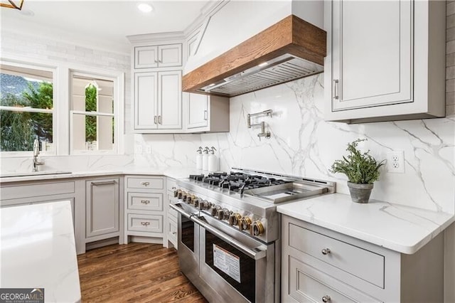 kitchen featuring decorative backsplash, dark wood-type flooring, custom range hood, range with two ovens, and sink