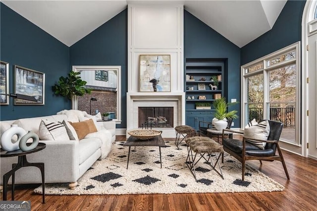 sitting room featuring high vaulted ceiling, built in features, wood-type flooring, and a fireplace